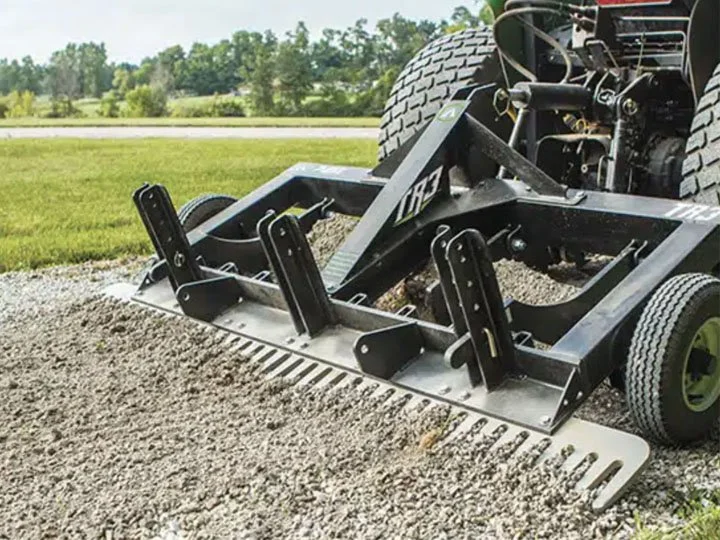 Close-up of a tractor equipped with a mechanical aerator attachment on a grassy field.