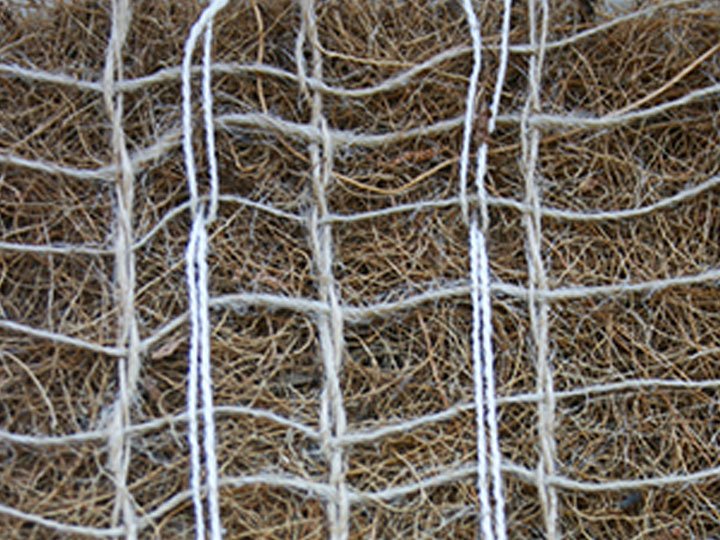 Close-up of a wire mesh fence with a dense mass of dried grass or hay behind it.