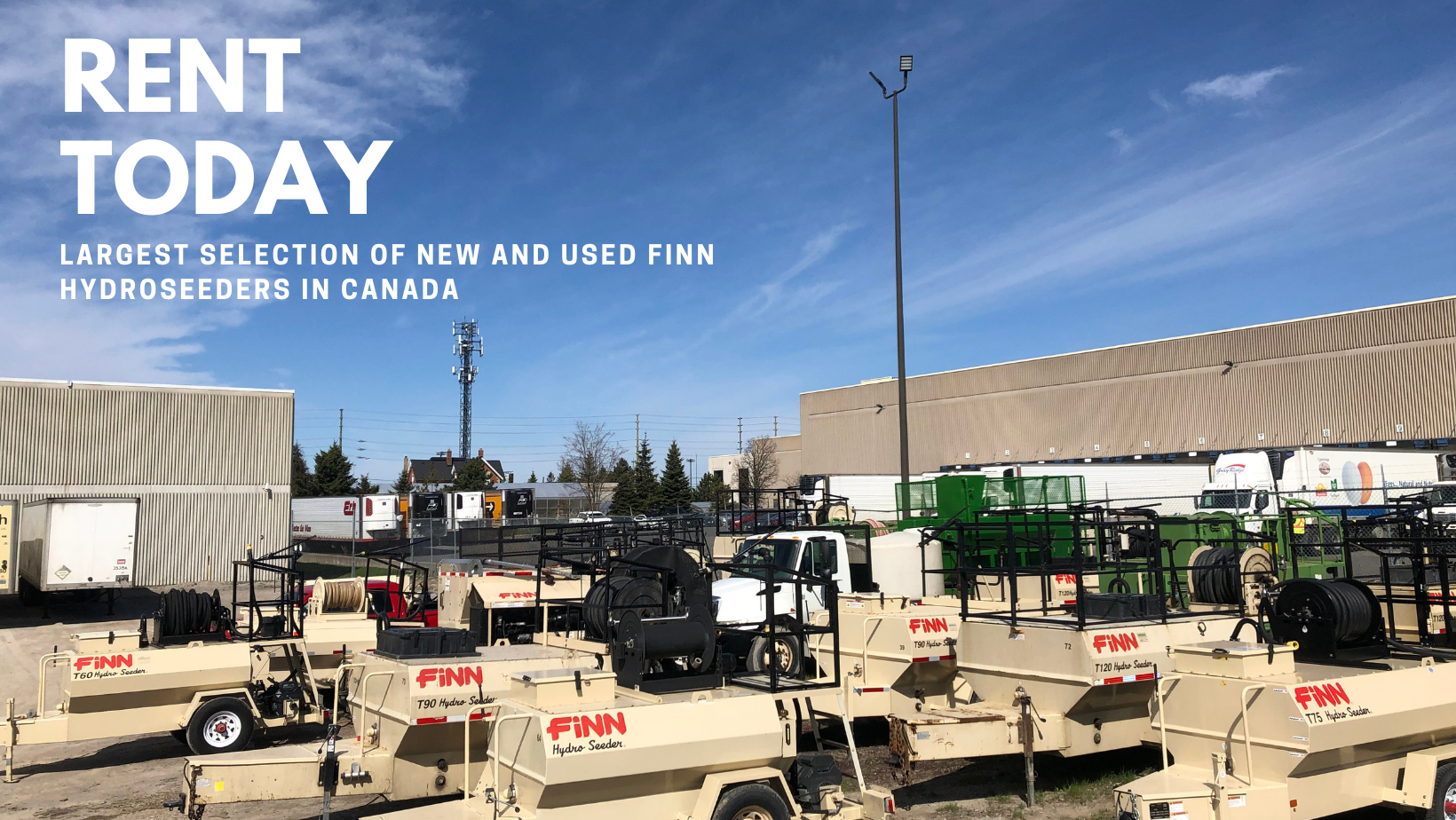 An outdoor lot with several hydroseeders and trucks parked against a backdrop of beige industrial buildings, blue sky, and a few trees.