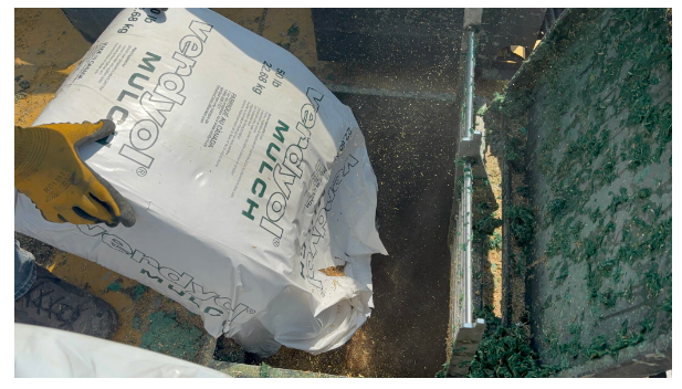 Person wearing yellow gloves holding a bag of roofing felt near a roof edge.
