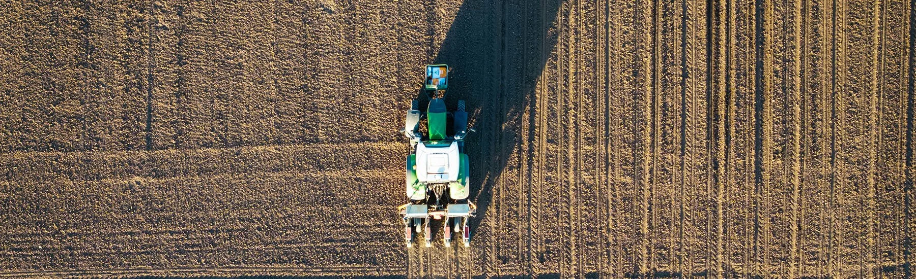 An aerial view of a tractor working in a field, planting or harvesting crops.