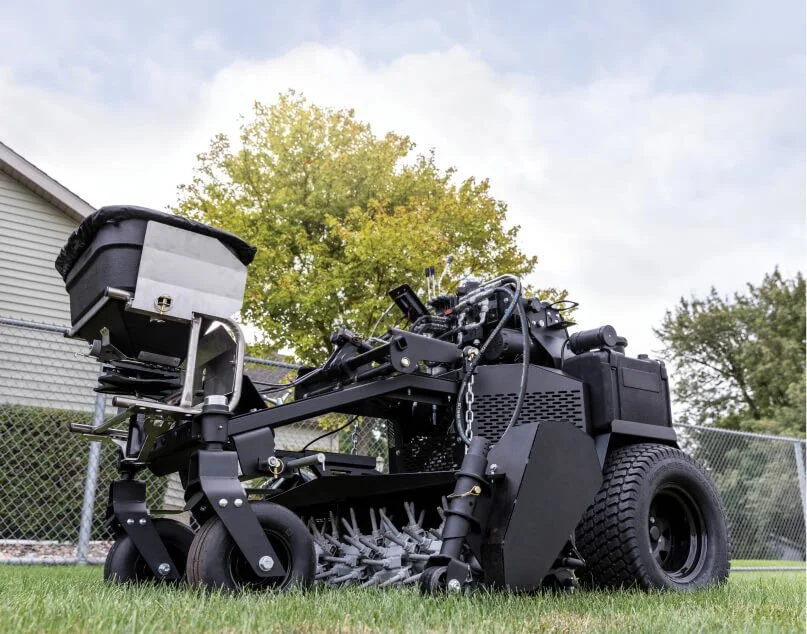 Self-driving mower robot on grass with a house and trees in background.