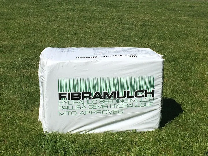 A white bag of Fibramuch hydraulic seeding mulch sitting on green grass.