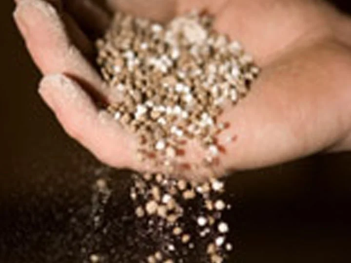A hand holding shiny, small, round beads with some falling out onto a dark surface.