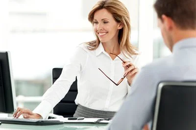 A businesswoman smiling and handing papers to a male colleague in an office setting.