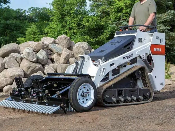 A compact bulldozer with a roller and track system, operated by a person, working on a construction site with rocks and dirt.