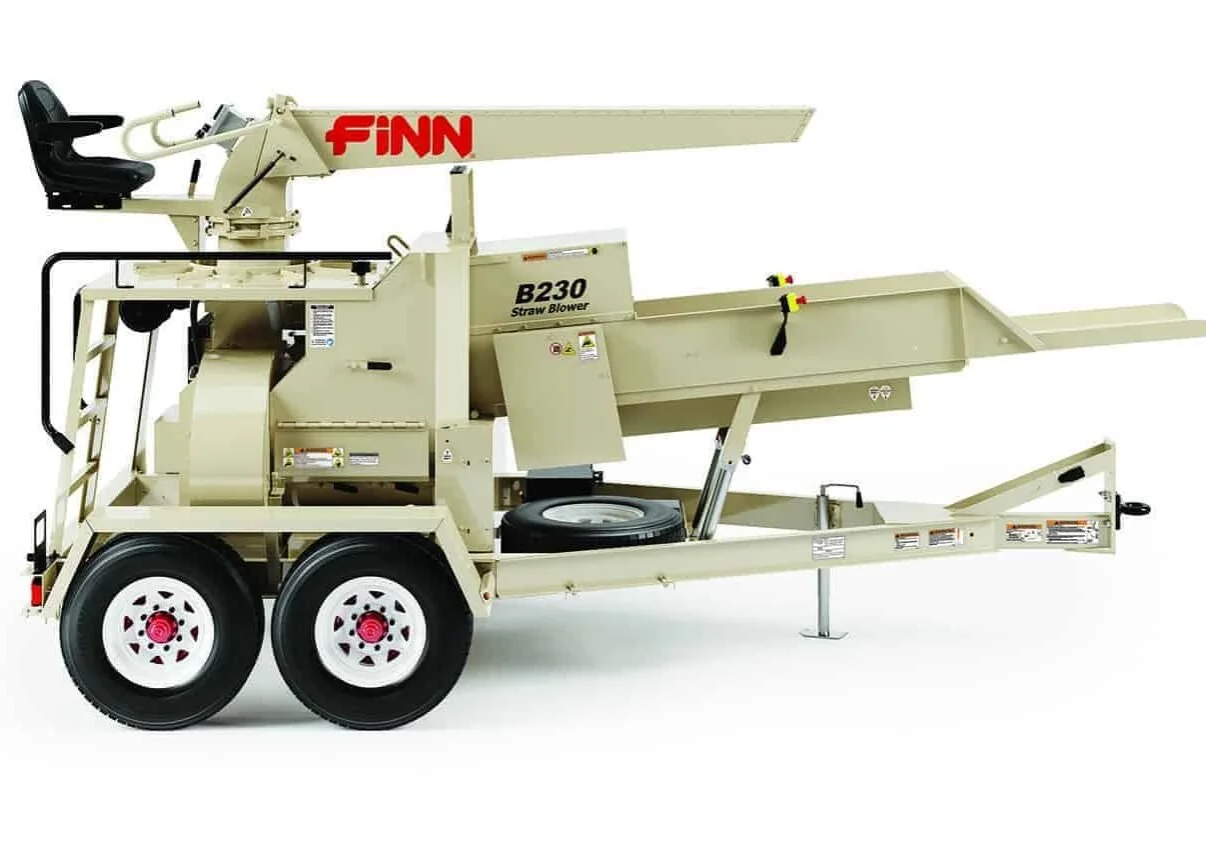 A beige Finn B230 straw blower machine with black and red accents, mounted on a two-wheel trailer, featuring a black seat, control panel, and extended arm.