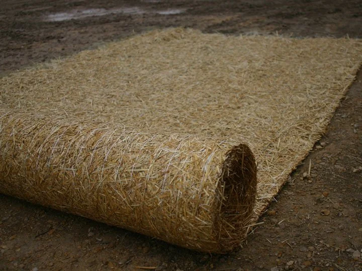A rolled-up section of straw or hay, placed on a dirt surface.