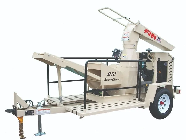 A large, beige mobile machine labeled "FNN B70 Straw Blower" with a conveyor system, protective railings, a control panel, and a wheel for towing, designed for blowing straw.