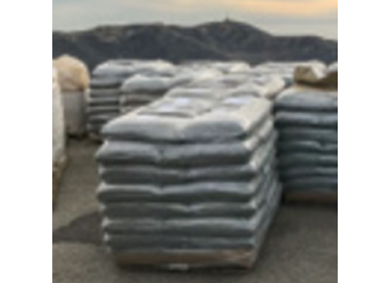 Stacks of large bags or bundles wrapped in plastic on a paved surface outdoors, with hills in the background.