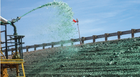 Irrigation sprinkler spraying water on a field with a wooden fence and a clear sky in the background.