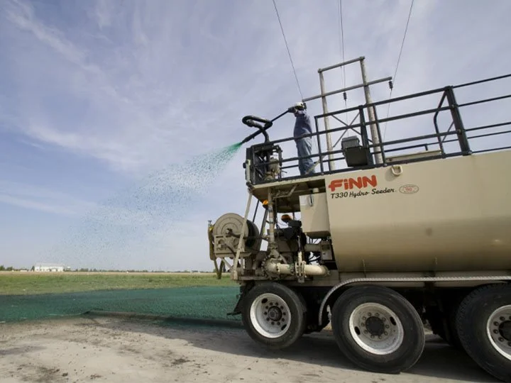 Worker on a large industrial fertilizer or seed spreader truck applying fertilizer or seed to a field.