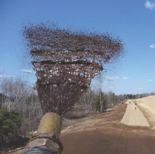 A mechanical broom sweeping dirt on a dirt road.