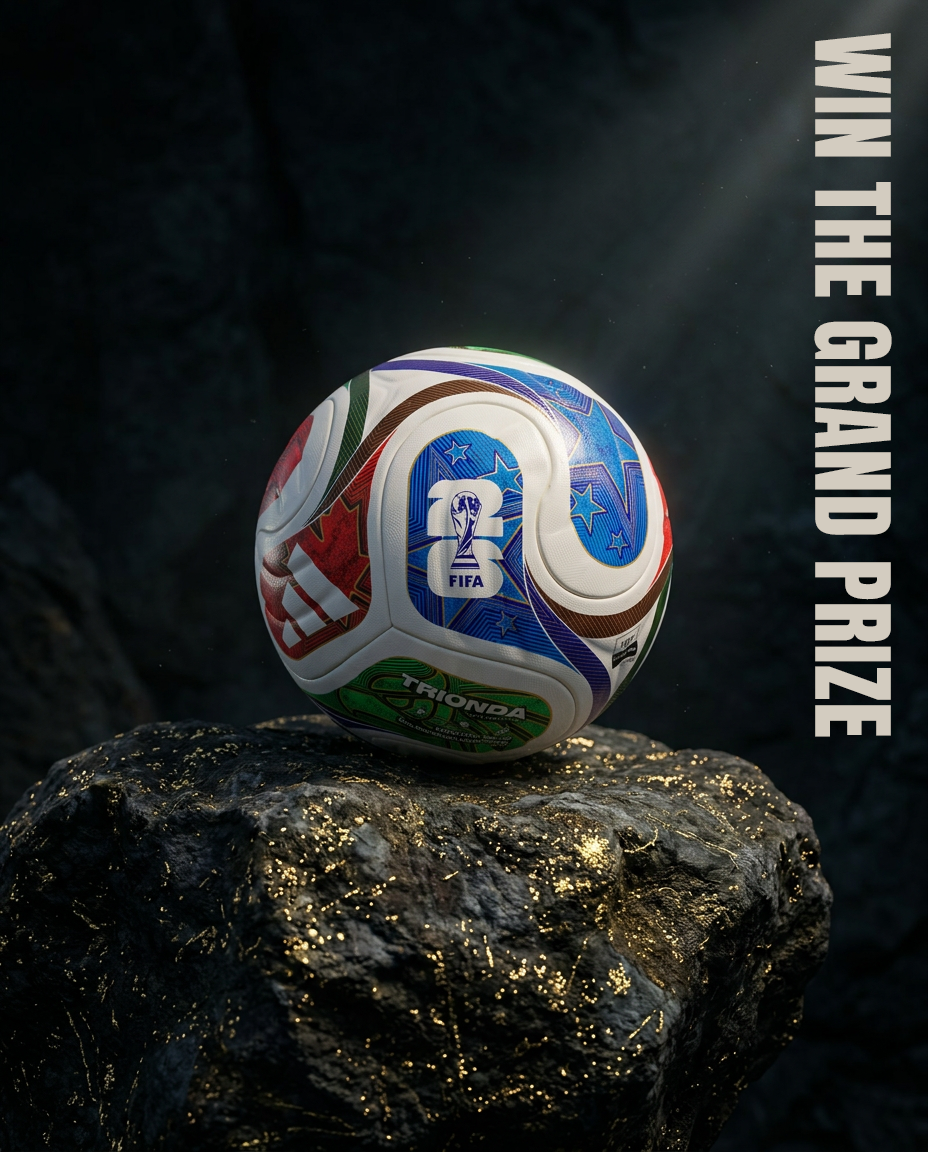 A colorful FIFA World Cup 2026 football with various patterns and logos, resting on a black rock with gold specks, illuminated by a spotlight with dark background and the text 'WIN THE GRAND PRIZE' written vertically on the right side.