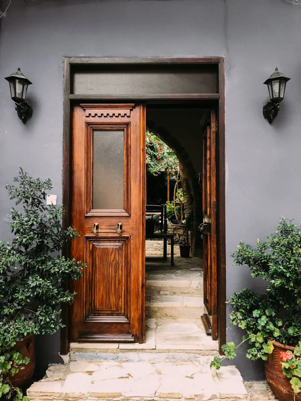 Open wooden door leading into a garden patio with potted plants and stone pathway.