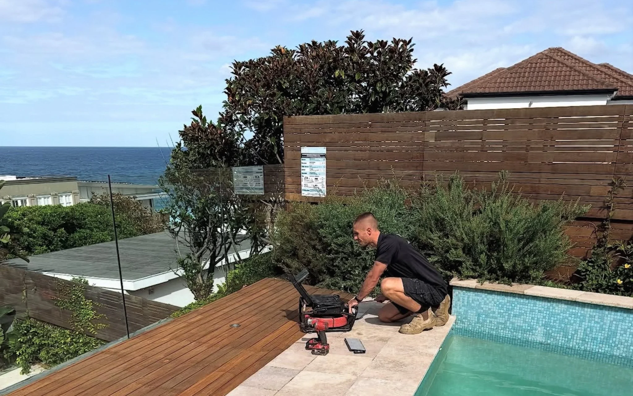 Jack from NewRise Plumbing carrying out plumbing work beside a residential swimming pool with CCTV drain inspection equipment.