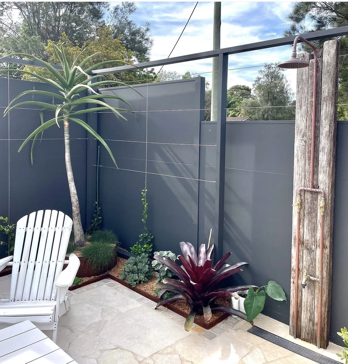 Custom outdoor shower in Woonona with reclaimed timber post, exposed copper pipework, rain shower head and sandstone paving.