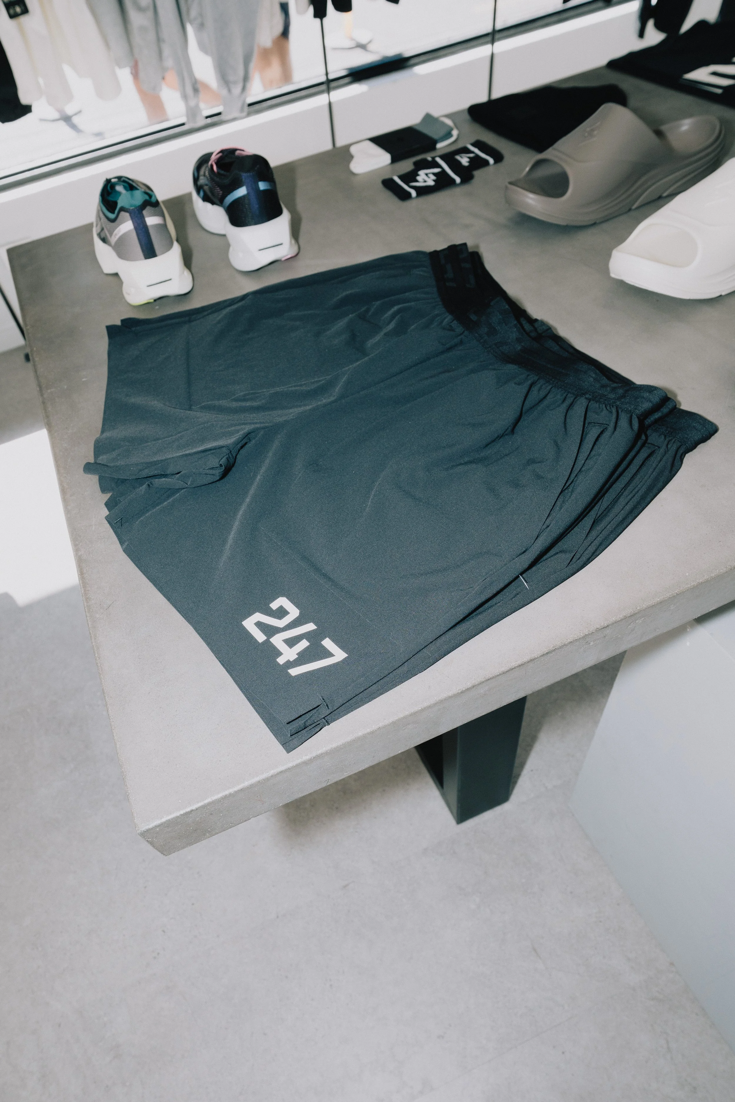 A display table with black athletic shorts, black and white socks, gray and beige slides, and white slides, with the number 247 on the shorts.