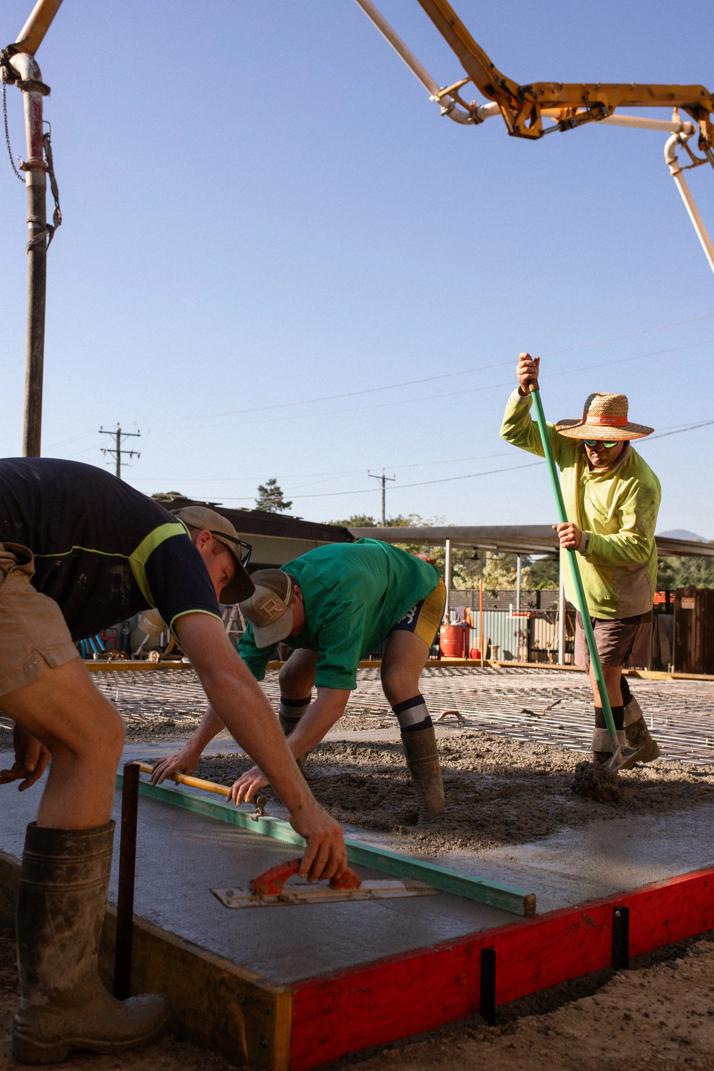 Construction workers smoothing freshly poured concrete at a construction site during daytime, with utility poles and equipment in the background.