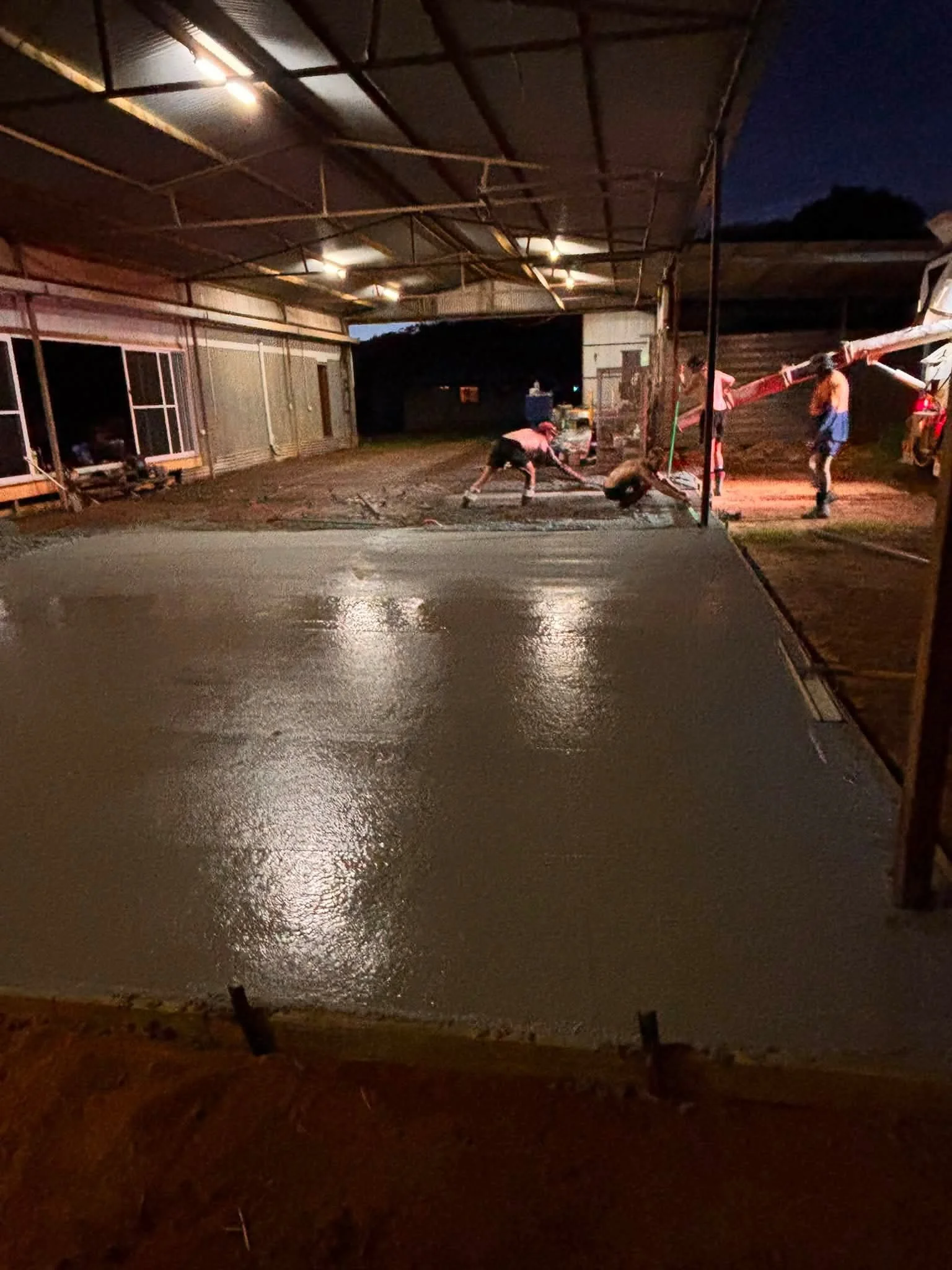 Construction workers pouring concrete on a building site at night, with a dark sky and unfinished structure in the background.
