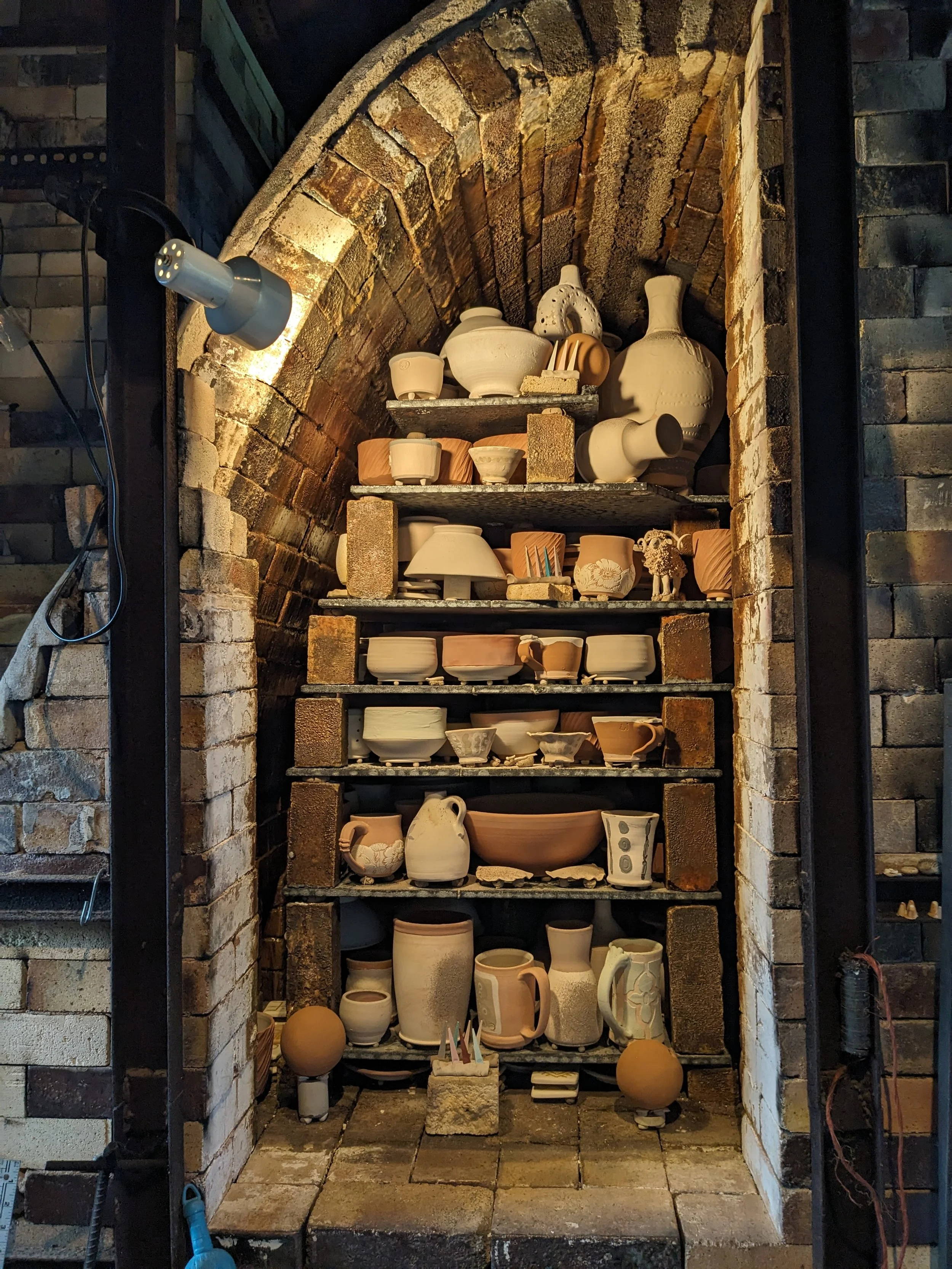 Ceramic vessels stacked on shelves inside a brick wood-fired kiln.