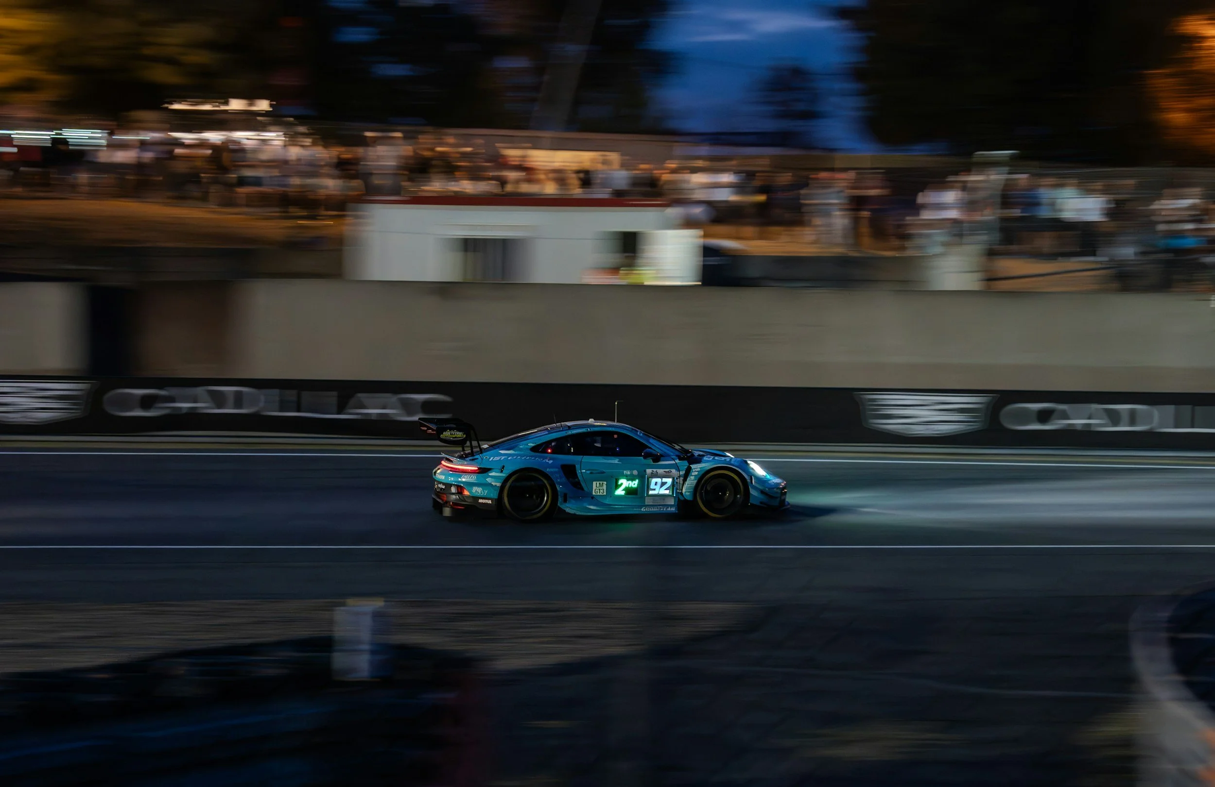 Une voiture de course bleue sur une piste lors d'une course nocturne, floue en arrière-plan.