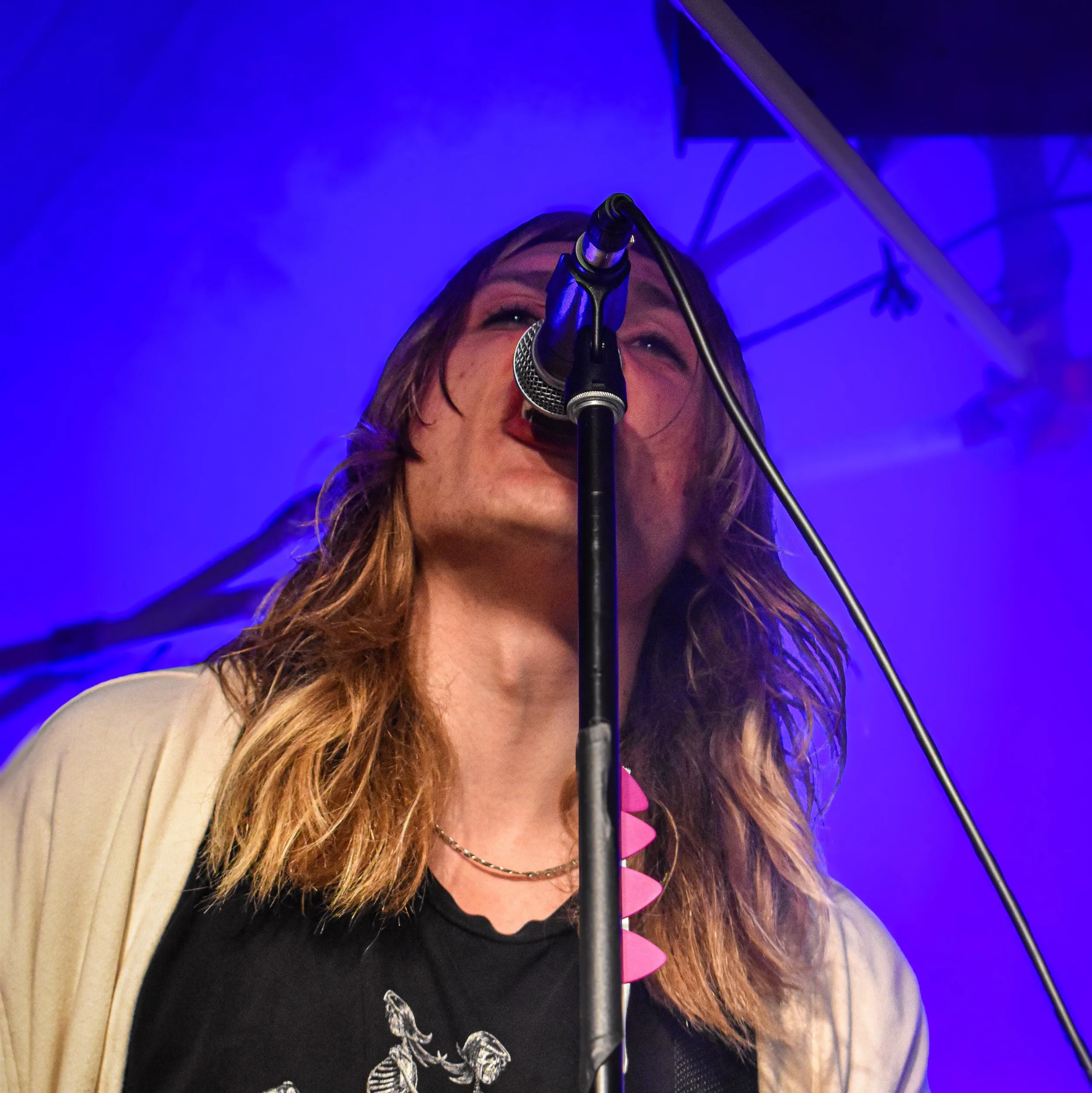 A woman with long hair singing into a microphone on stage with blue and purple lighting.