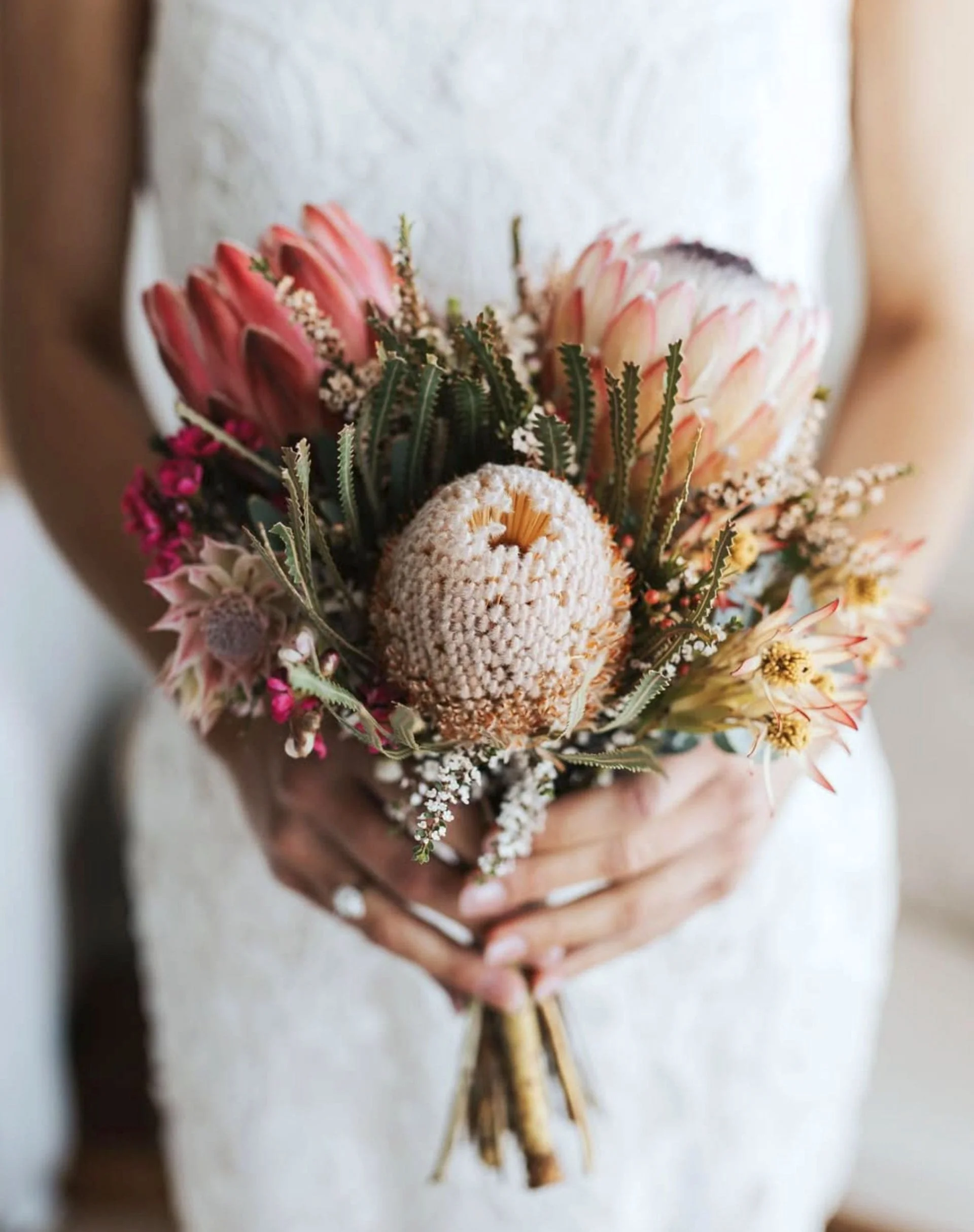 Person holding a bouquet of pink, white, and green flowers with textured flower heads and green foliage.
