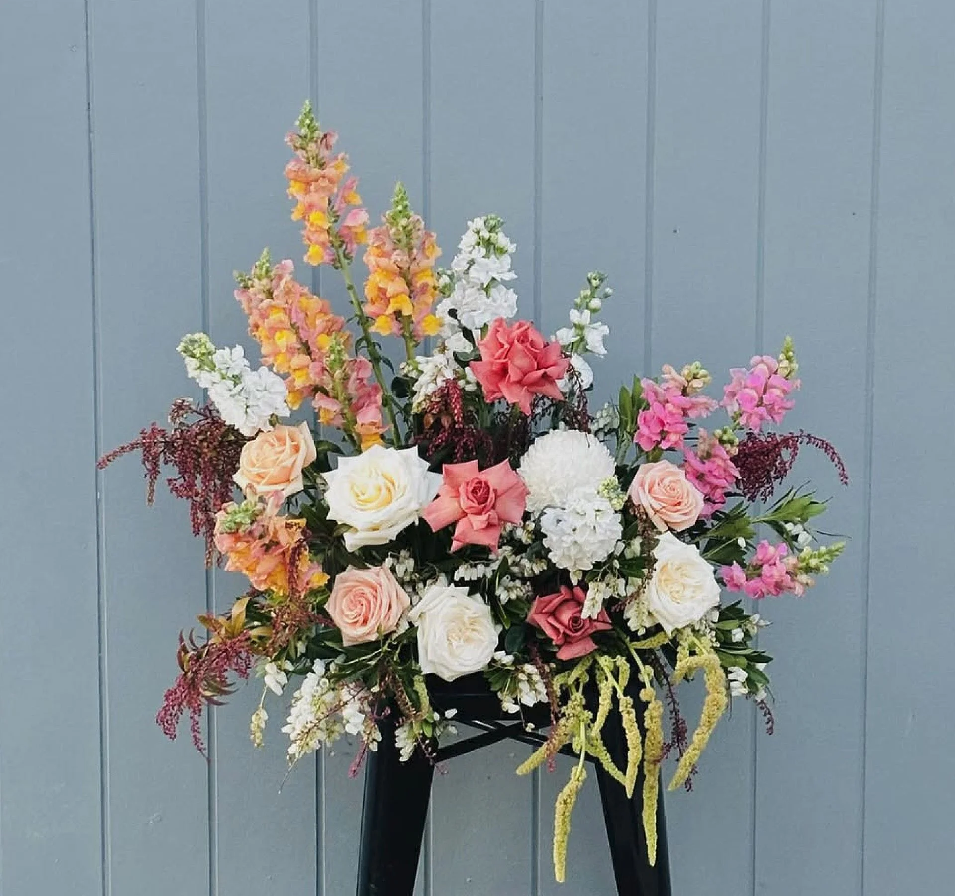 A colorful flower arrangement with various pink, white, yellow, and purple flowers against a blue wooden wall background.