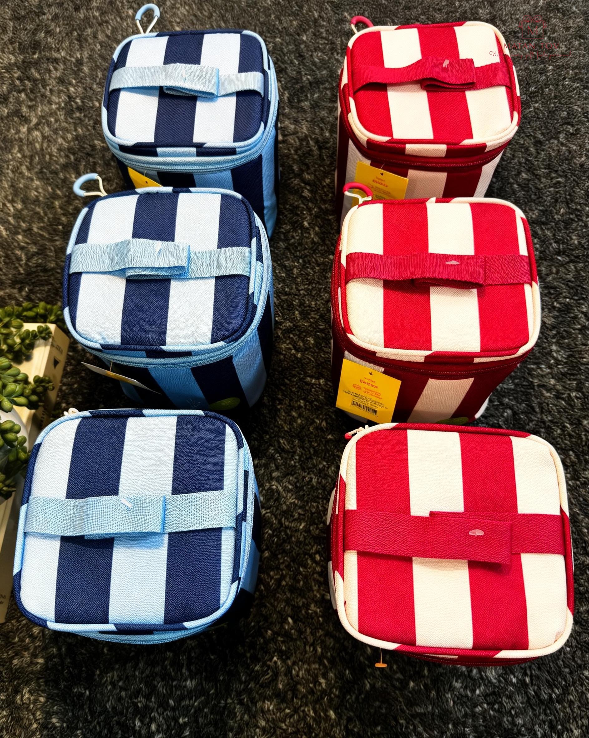 Two red and white striped insulated lunch bags and two blue and white striped lunch bags on a black carpeted surface.