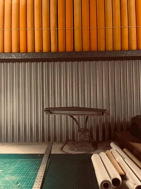 Interior space with wooden and corrugated metal walls, a small brown table, rolls of paper, and a cutting mat.