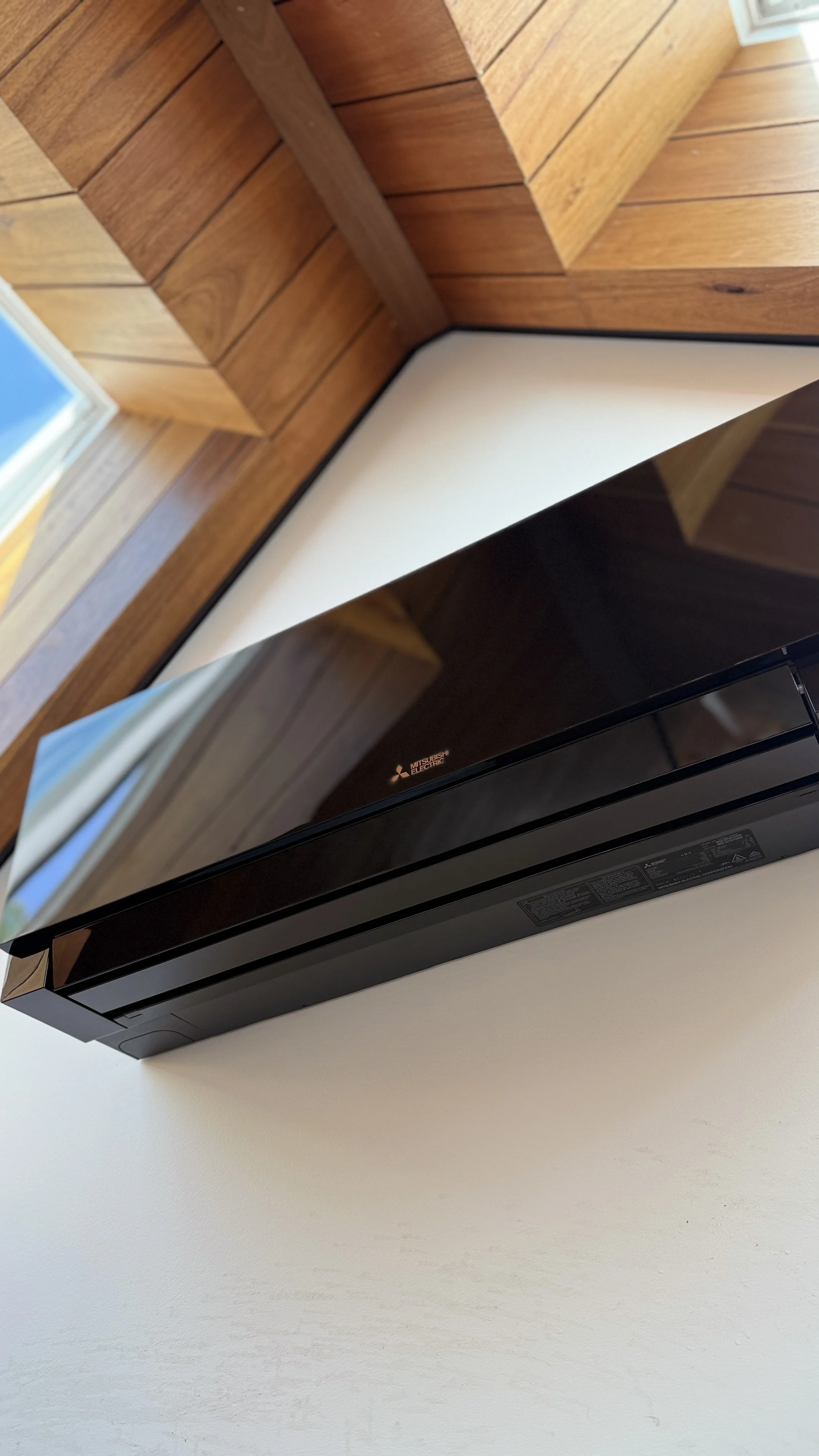Black Mitsubishi Electric microwave oven mounted on a white wall below a window with wooden framing.