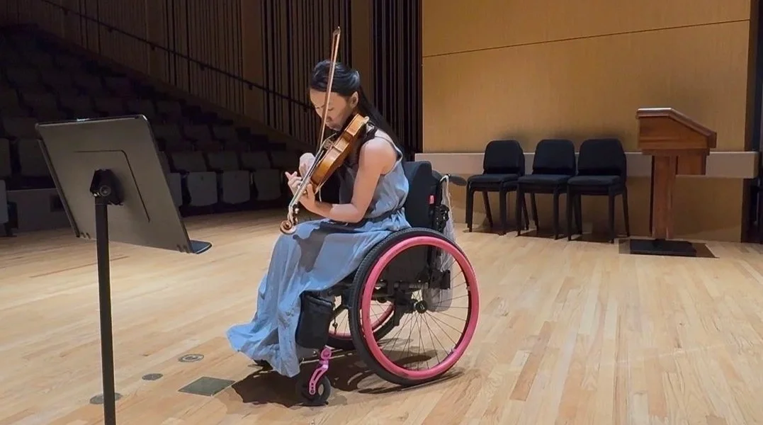 A woman in a wheelchair playing a violin in a concert hall.