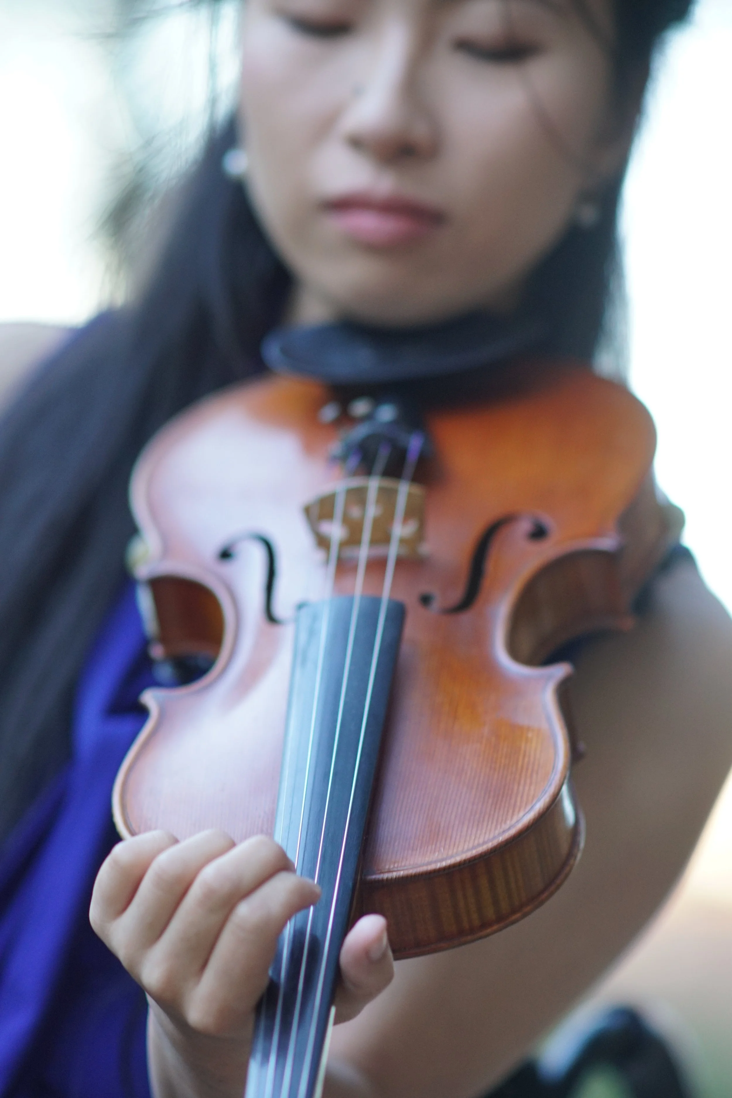 A young girl playing the violin outdoors, focusing on her hand on the strings and the violin's body.
