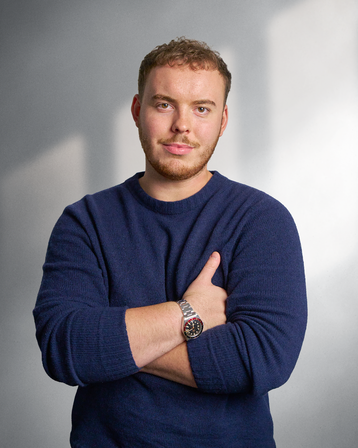 Man standing, smiling in blue sweater with sunlight in background
