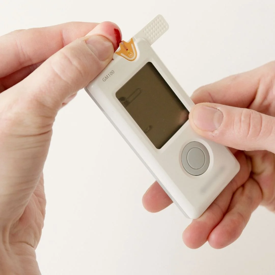 Person holding a blood glucose meter with a test strip being inserted.
