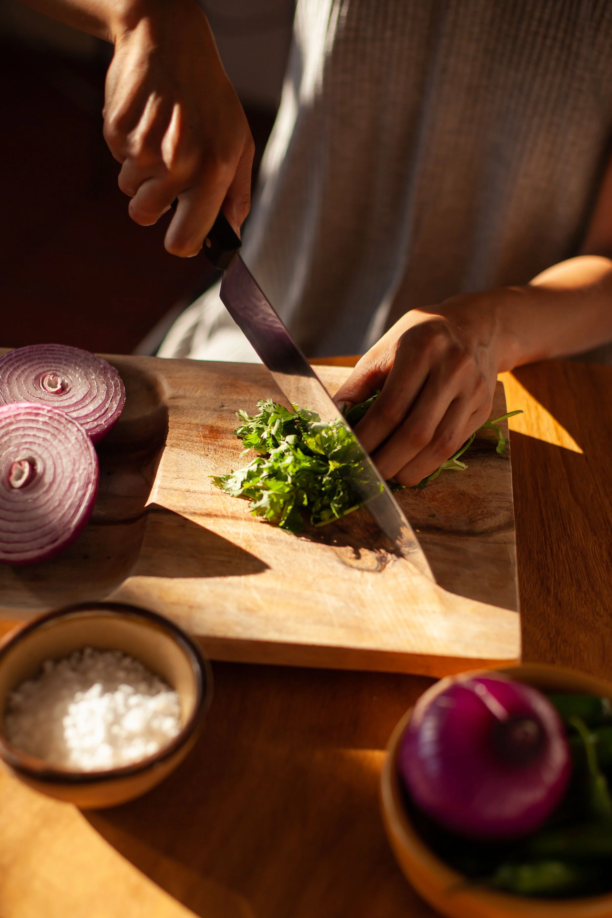 Sliced red onions on a wooden cutting board, with cilantro and small bowls of salt and pepper nearby.
