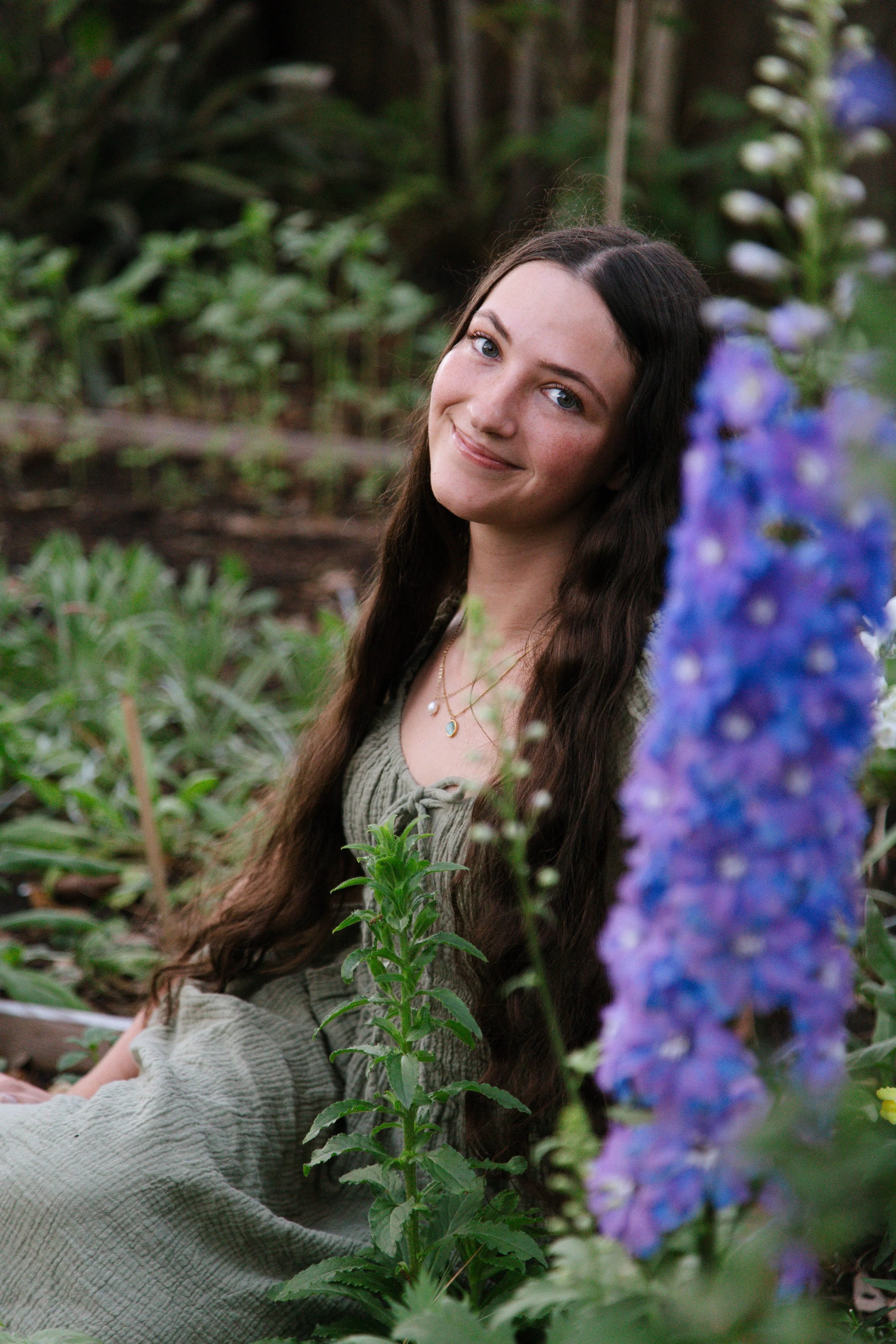 A picture of a girl sitting with a purple delphinium flower