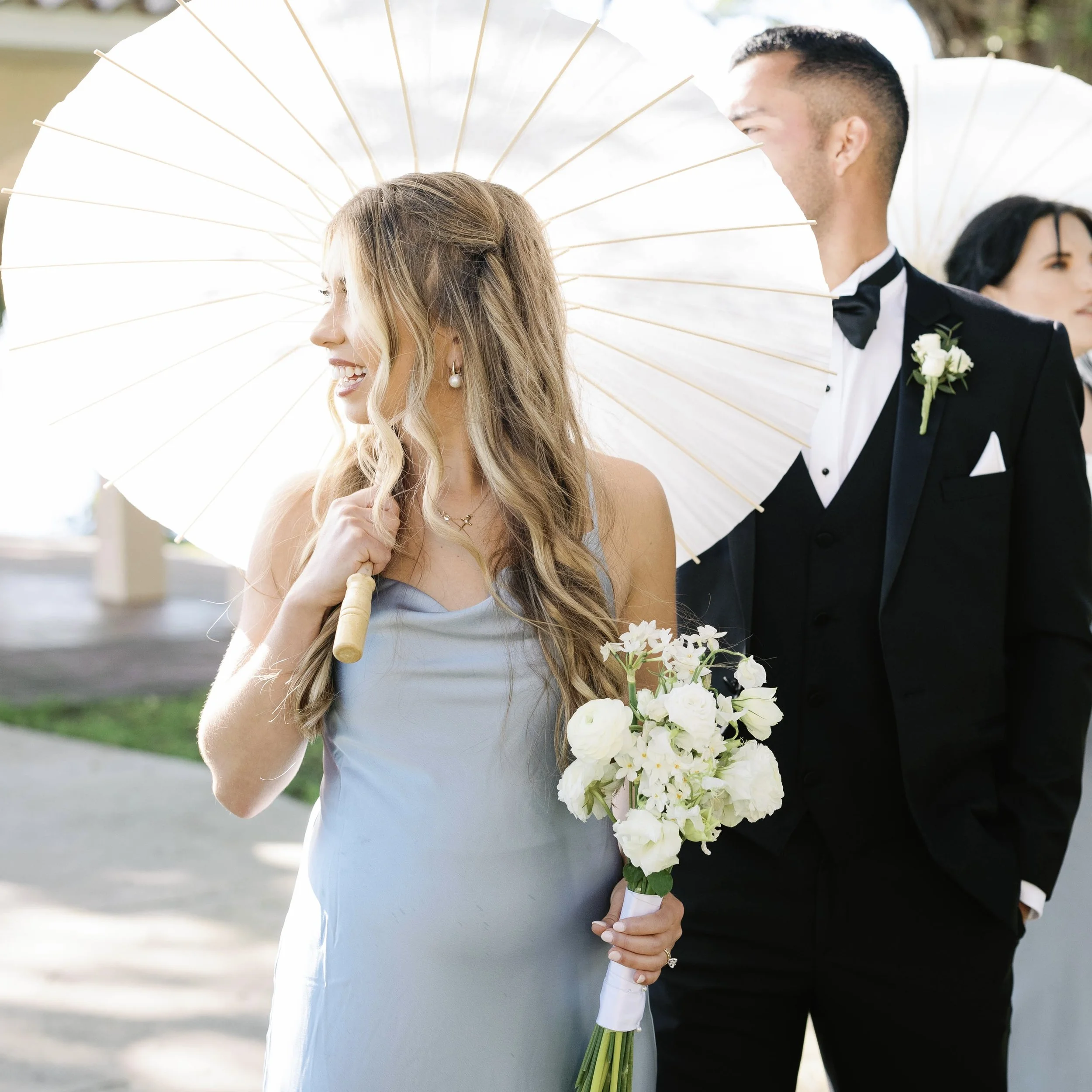 A bridesmaid at a wedding with an umbrella and bouquet