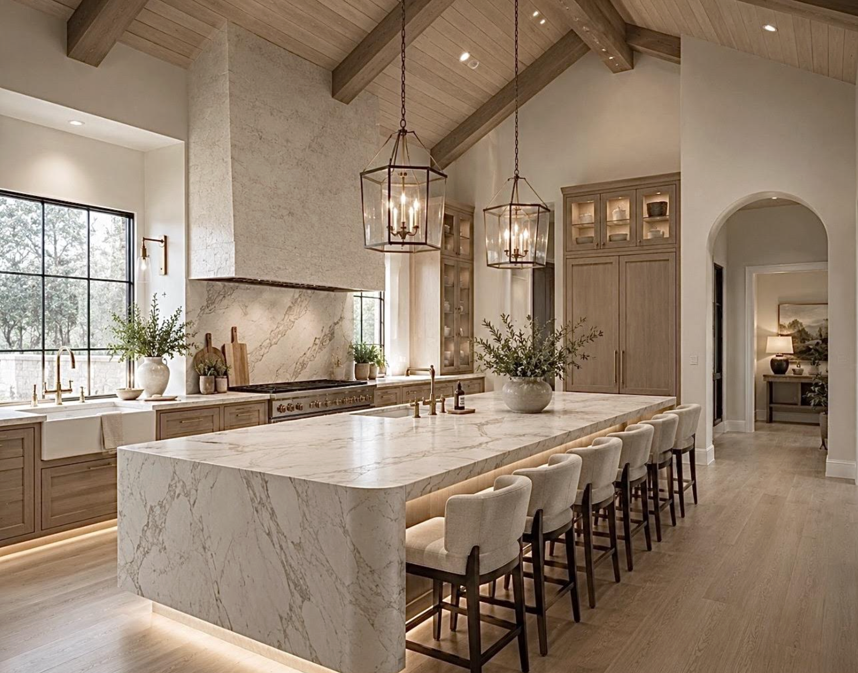 Modern kitchen with a large marble island, beige cabinetry, a vaulted wooden ceiling with pendant lights, and a window with natural light.