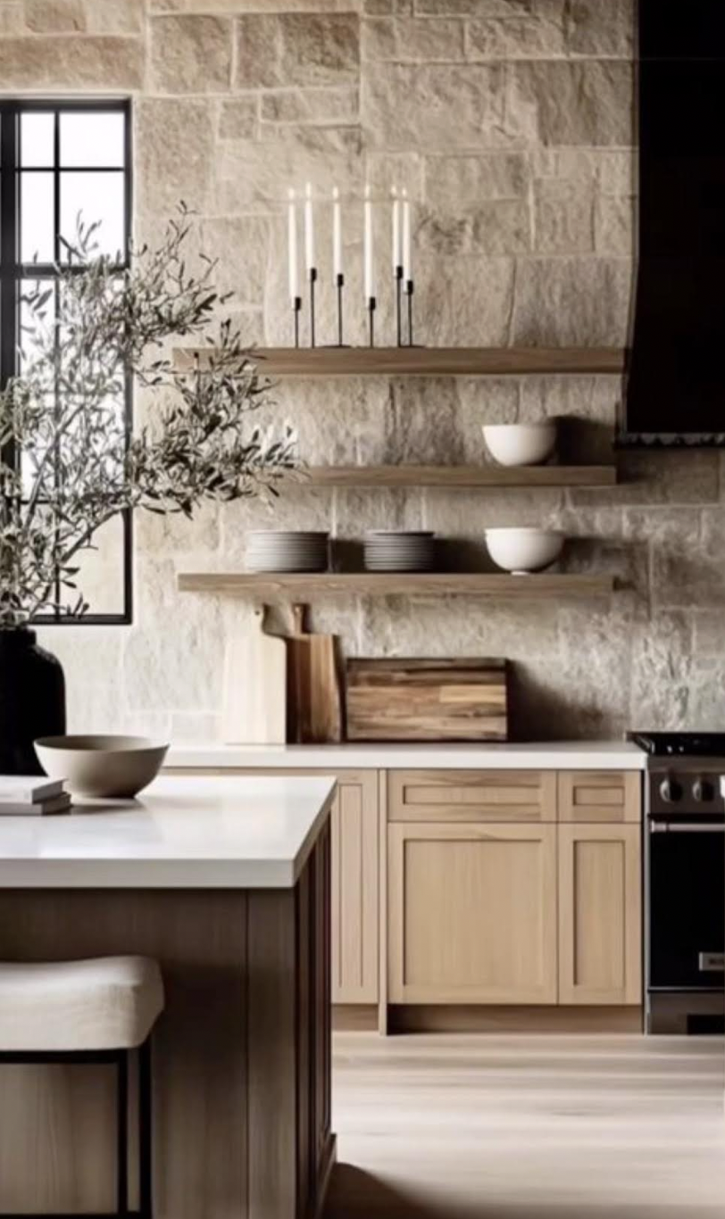 A kitchen with a stone wall, open wooden shelves holding white bowls, gray plates, a wooden cutting board, and a black stove. A window with a black frame and a potted plant on the counter are also visible.