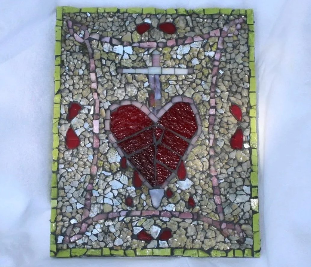Mosaic art piece depicting a broken heart with a sword through it, dripping blood, framed by small green tiles, with a white glass mosaic background.