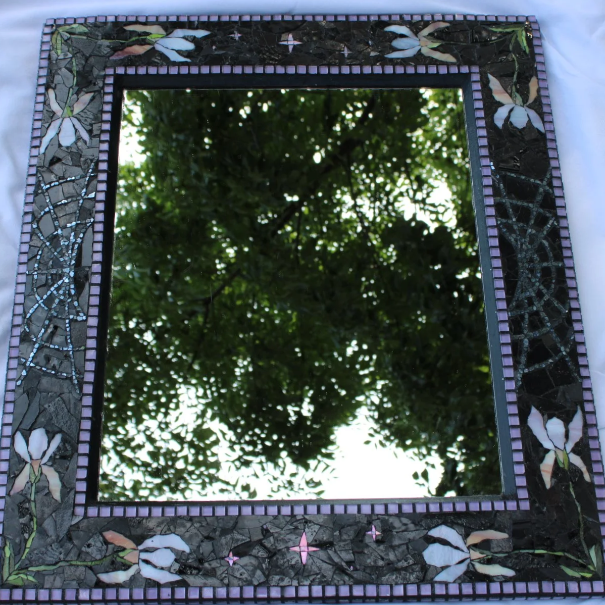 Decorative mosaic mirror reflecting tree branches and leaves.