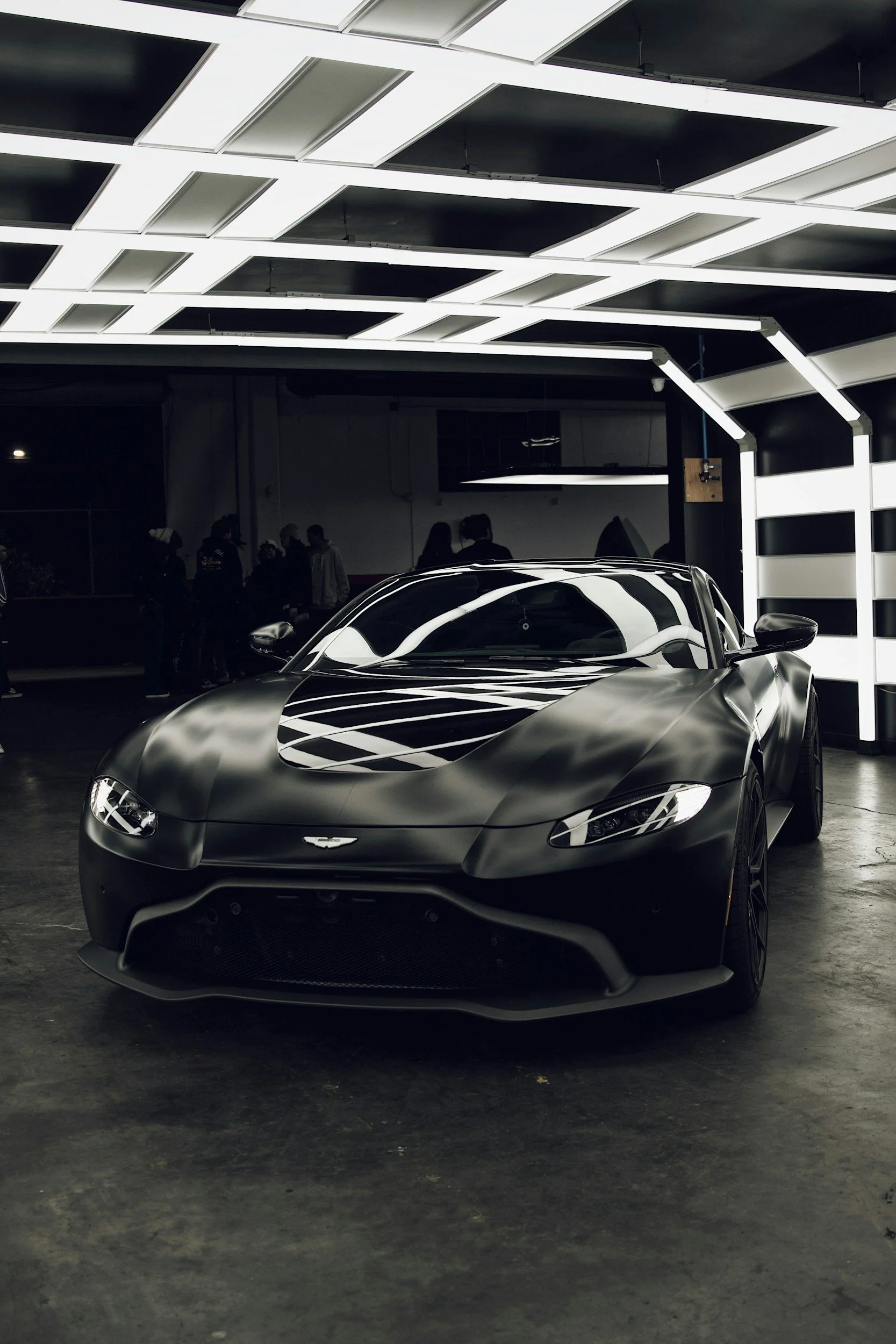 A sleek, shiny black sports car with reflective surfaces parked in an indoor showroom with modern lighting fixtures.