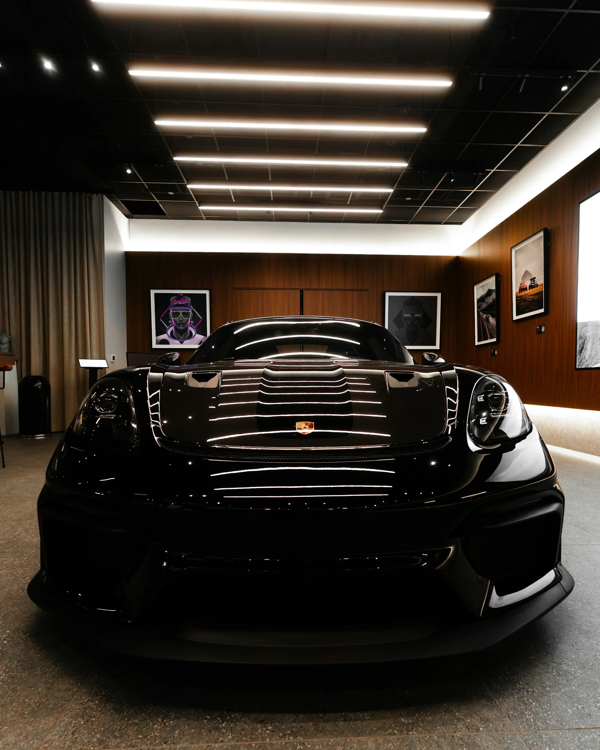 Front view of a sleek, black Porsche sports car inside a modern showroom with artwork on the walls and ceiling lighting. - Porsche Modesta Ceramic Coatings