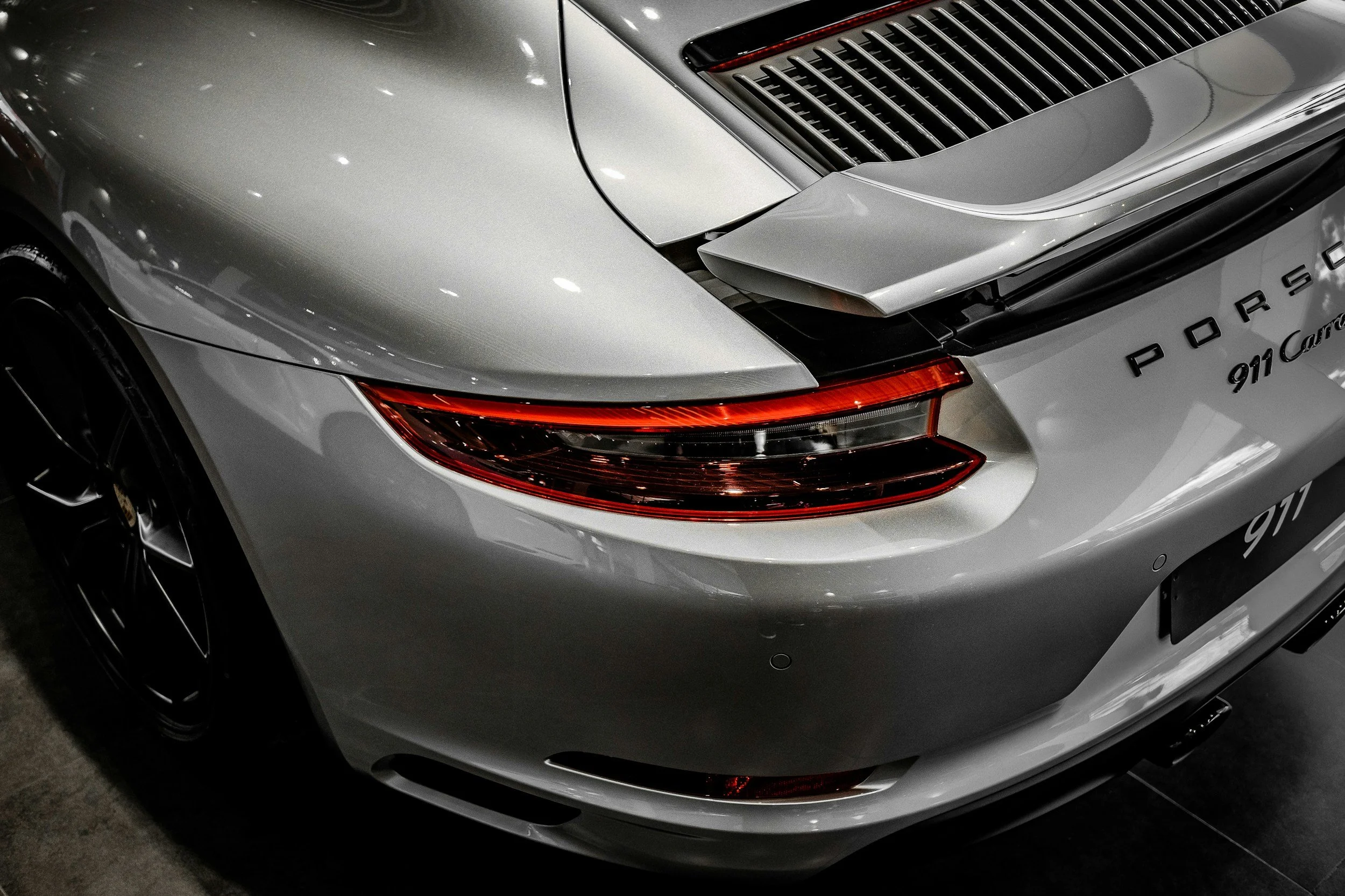 Close-up of the front and side of a silver Porsche 911 Carrera with sleek design and red tail lights. - luxury auto reflection