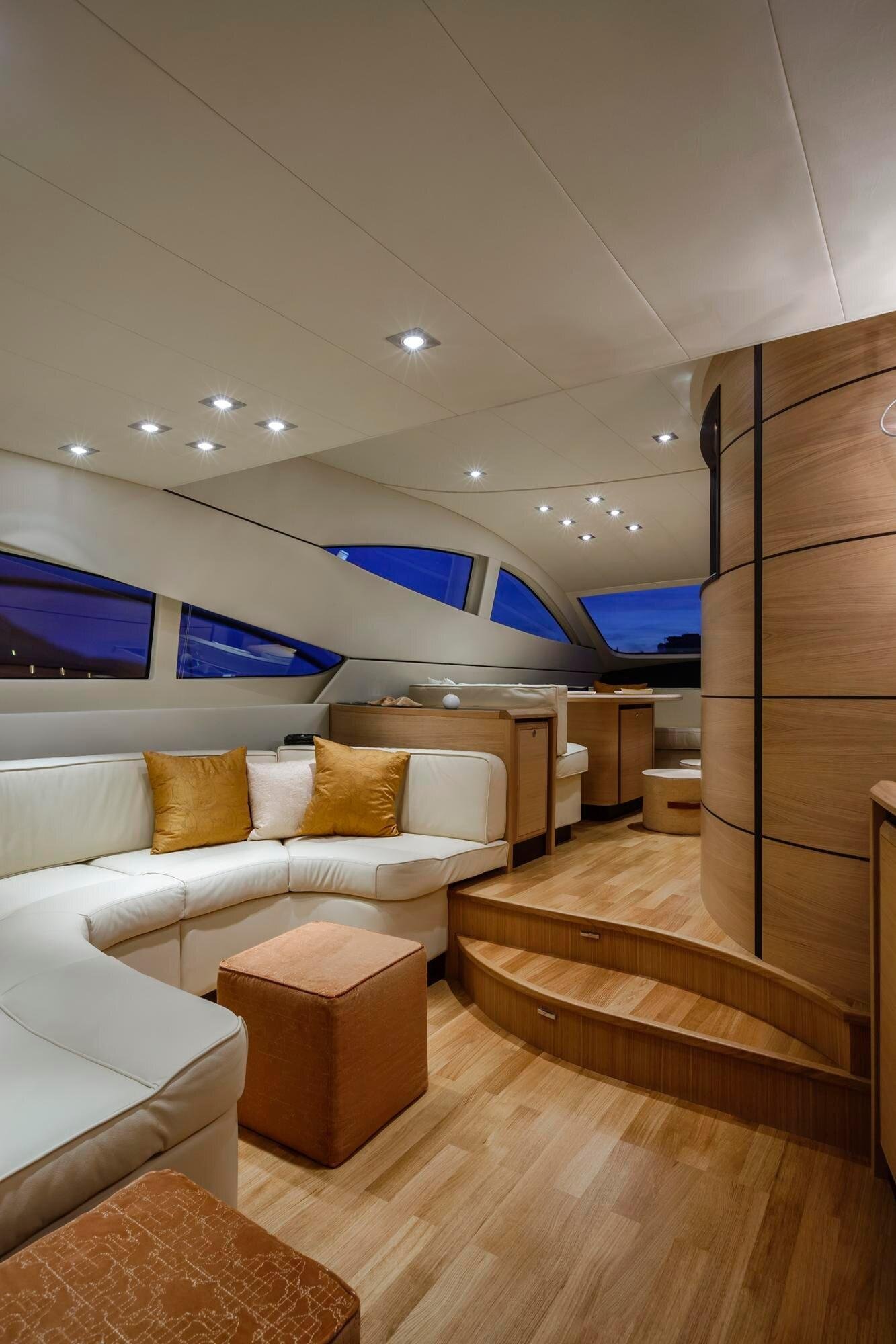Interior of a yacht or modern home with curved wooden walls, large windows, white seating with orange pillows, and wooden flooring. Recessed ceiling lights provide illumination. - Marine Detailing Cleveland