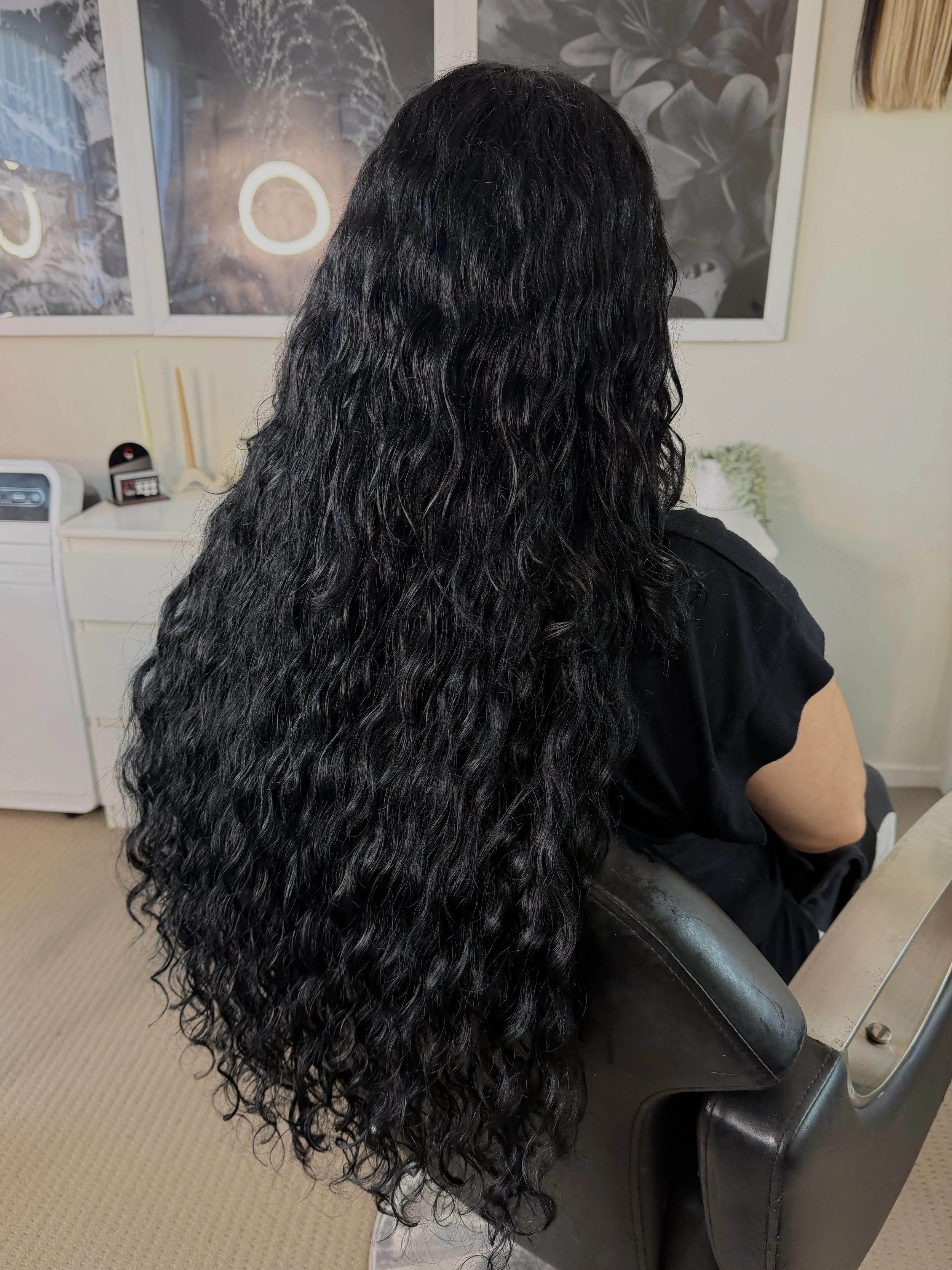 Long, wavy jet black hair extensions, seamlessly blended for a flawless, naturally elevated finish.