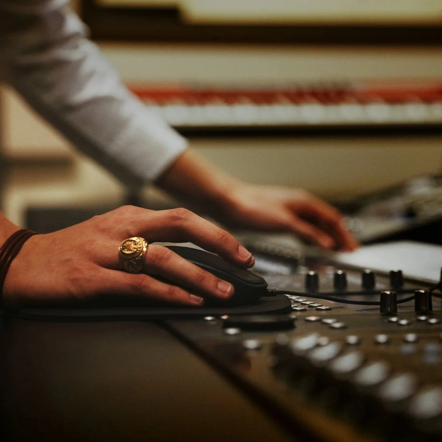 A person wearing a gold ring on mixing console with their right hand, with their left hand reaching towards the controls in the background.