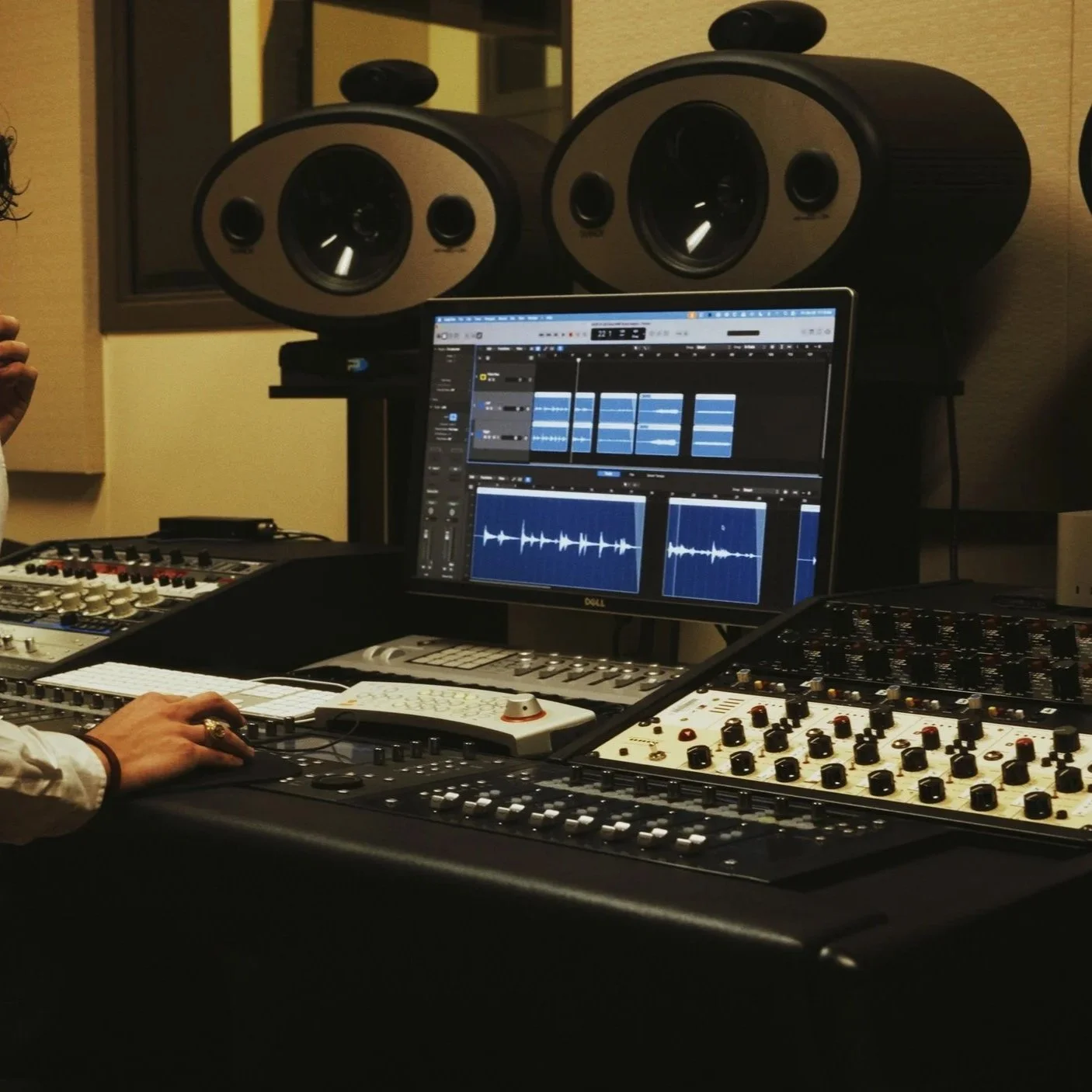 A music producer working in a studio surrounded by studio monitors, a computer with digital audio workstation software, and various audio equipment.